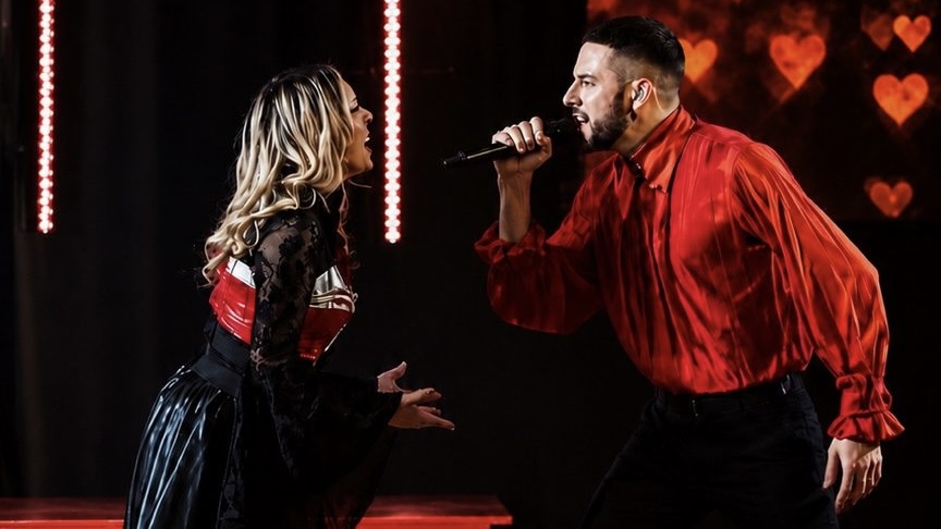 Deux artistes du Cabaret Dory Arena sur scène : un chanteur en chemise rouge tenant un microphone face à une artiste en costume noir et rouge.